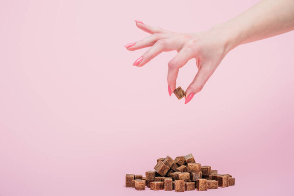 обрезанный взгляд женщины с горсткой белых кубиков сахара на изолированных на розовый
