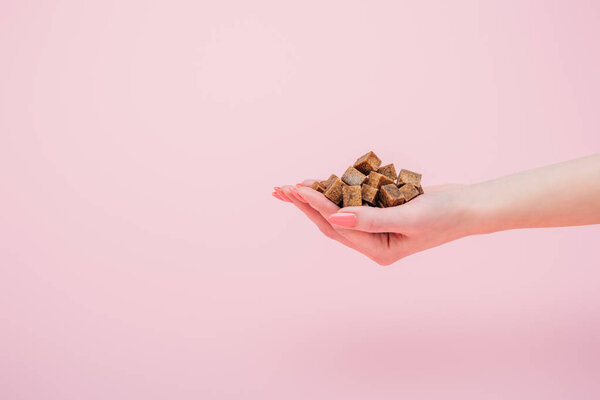 обрезанный вид женщины с горсткой коричневых кубиков сахара изолированы на розовый
