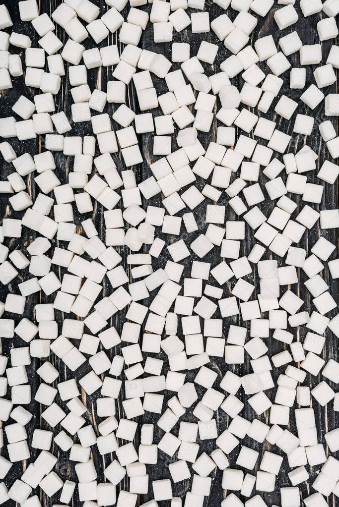 top view of white sugar cubes on black wooden surface 