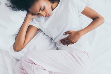 yatakta yatarken mide ağrısı çeken güzel afro-amerikan kadın