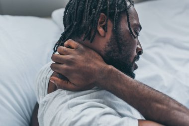 Yatak odasında boynu ağrıyan Afrikalı Amerikalı genç bir adam.