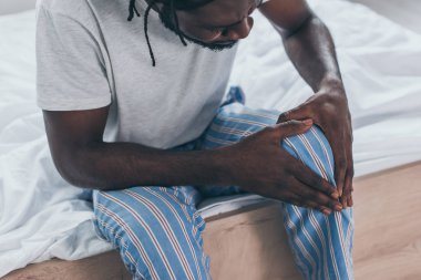 yatak odasında diz ağrısı muzdarip genç Afrikalı adam kırpılmış görünümü