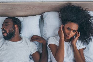 horlama kocası yakınında yatakta yatarken baş ağrısı muzdarip Afrikalı Amerikalı kadın üst görünümü