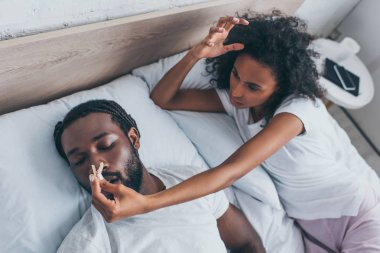 young african american woman pinning nose of snoring husband  clipart