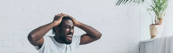 寝室で頭痛に苦しんでいる間に叫ぶアフリカ系アメリカ人の男性のパノラマショット — ストック写真