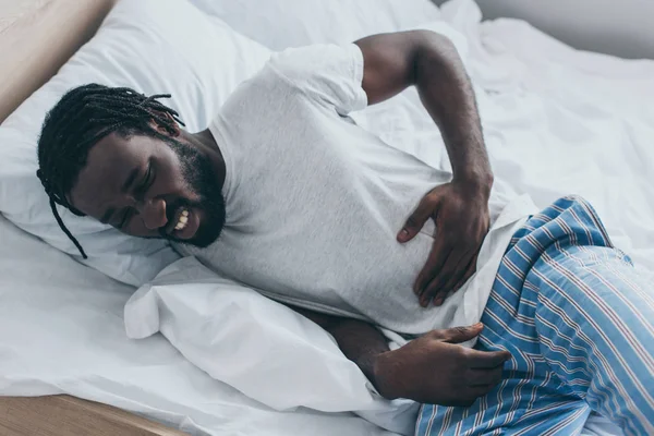 Olycklig Afrikansk Amerikansk Man Som Lider Buksmärtor Medan Liggande Sängen — Stockfoto
