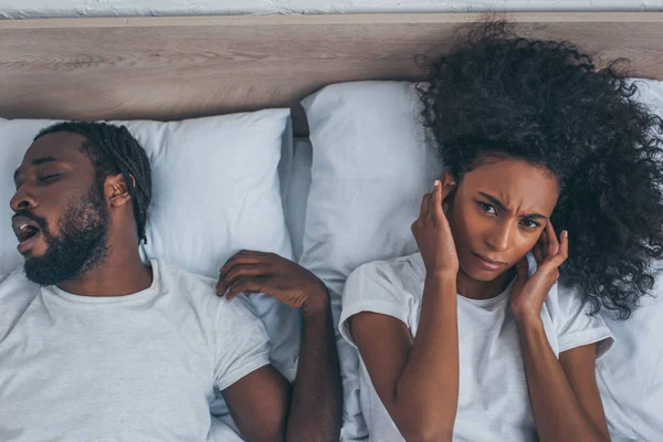 非洲美国妇女头痛 而躺在床上打鼾丈夫的顶视图 — 图库照片