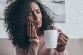 unglückliche afrikanisch-amerikanische Frau leidet unter Zahnschmerzen und hält Kaffeetasse