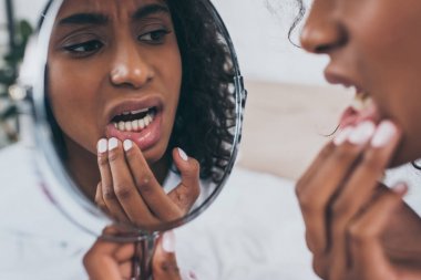 young african american woman looking at mirror while suffering from tooth pain clipart