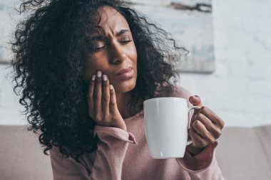 mutsuz afrikalı Amerikalı kadın diş ağrısı muzdarip ve kahve fincanı tutarak