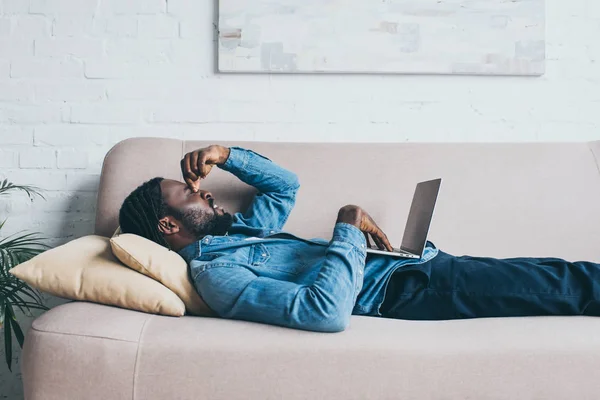 Unavený Afroamerický Muž Trpící Bolestí Hlavy Při Lhaní Pohovce Laptopem — Stock fotografie