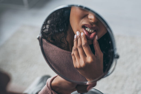 partial view of african american woman looking at mirror while suffering from toothache