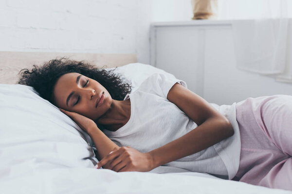 pretty african american woman in pajamas sleeping on white bedding