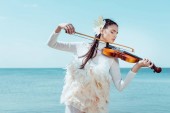 gyengéd nő fehér hattyú jelmezes játszik a hegedűre