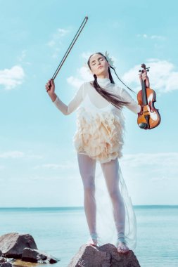 beautiful woman in white swan costume standing on river background with violin  clipart