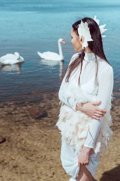 brunette woman in white swan costume standing near pond, looking at birds