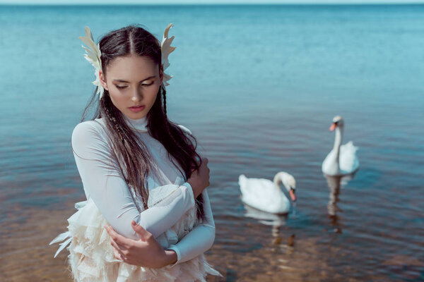 tender woman in white swan costume closing eyes, standing near river with birds
