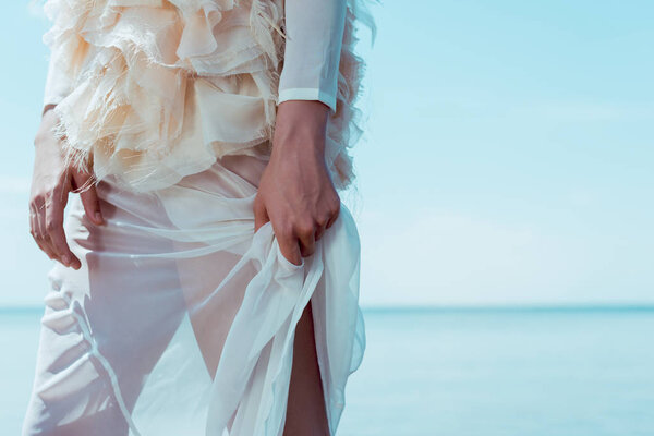 cropped view of adult woman in white swan costume standing on blue sky background