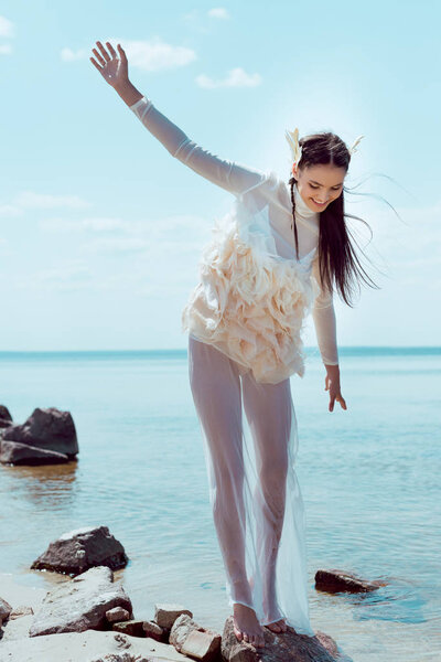 happy brunette woman in white swan costume standing on rock near river