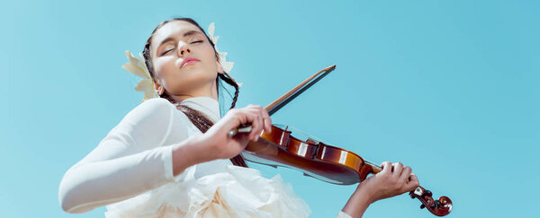 low angle view of tender woman in white swan costume standing on blue sky background with violin