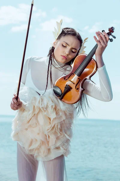 白い白鳥の衣装を着た優しい女性がバイオリンで青空の背景に立っている — ストック写真