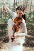 elegáns nő fehér hattyú jelmez állva az erdő háttérben, hegedűre játszik