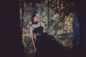 selektivní zaměření krásné ženy na kostým černé čarodějnice stojící mezi stromy