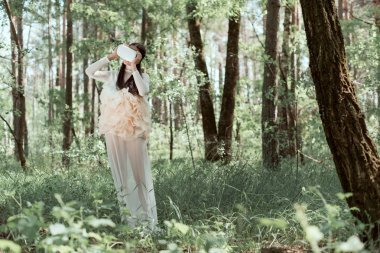 tender woman in white swan costume and vr headset standing on forest background clipart