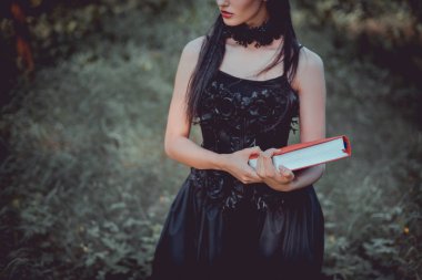 kırmızı kitap ile orman arka planda duran cadı kostümlü kadın kırpılmış görünümü