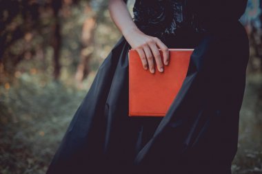 cropped view of adult woman in witch costume standing with red book clipart
