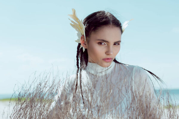 brunette woman in white swan costume standing near dry bush, looking at camera