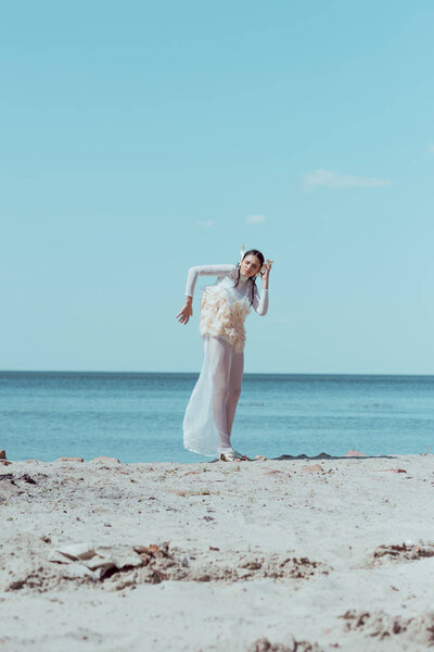 tender woman in white swan costume standing on sandy beach