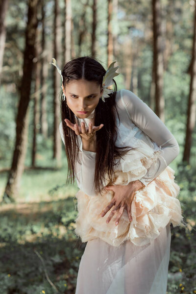 mad woman in white swan costume standing on forest background, looking at camera