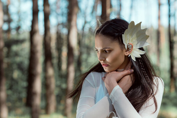 beautiful woman in white swan costume looking away, holding hands on neck