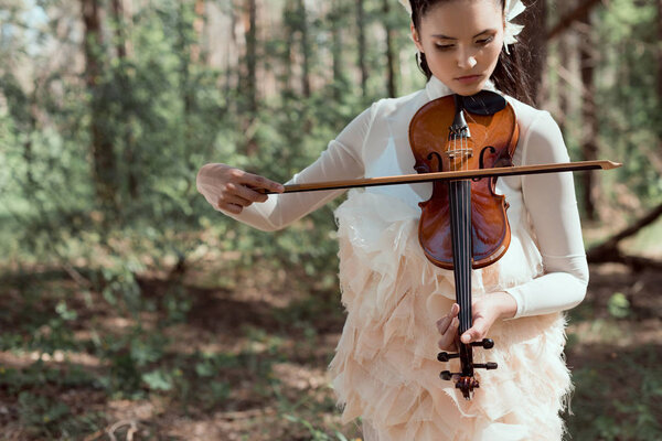 young woman in white swan costume standing on forest background with violin