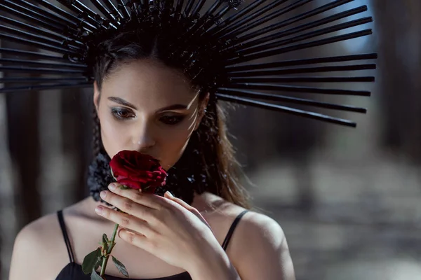 顔の近くに赤いバラを持つ頭の上に王冠を持つ魔女の衣装を着た若い女性の肖像画 — ストック写真