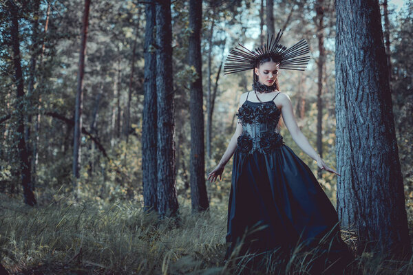 красивая женщина в костюме ведьмы гуляет по лесу, смотрит в сторону
