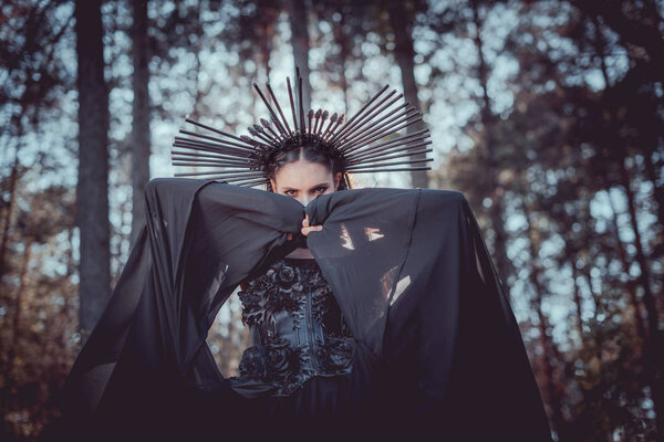 low angle view of woman in witch costume with crown on head covering face black textile