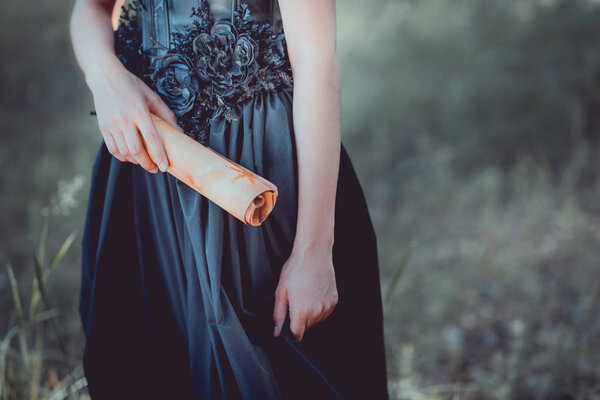 cropped view of woman in black witch costume standing with scroll in hand