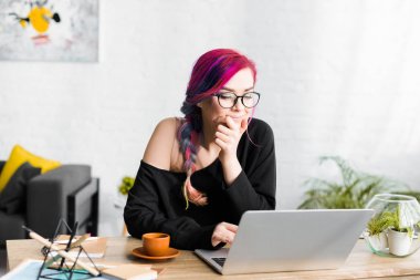 renkli saçlı hipster kız masanın arkasında oturan ve dizüstü pensively bakarak