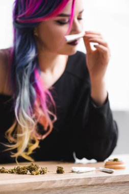selective focus of beautiful hipster girl with colorful hair sniffing joint with weed clipart
