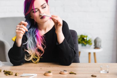  beautiful hipster girl with colorful hair sniffing joint with weed clipart