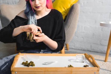 girl closing herb grinder with medical cannabis sitting on floor in living room clipart