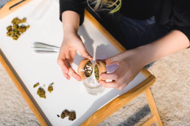 ahşap tepsi üzerinde cam marihuana öğütücüden otlar koyarak kız üst görünümü