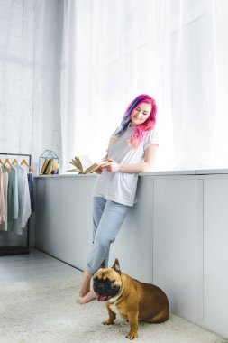 renkli saç kitap tutan ve Fransız bulldog bakarak güzel kız