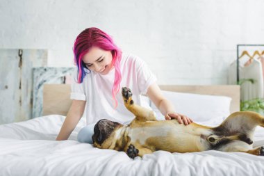 renkli saç petting ile kız ve yatakta geri döşeme sevimli fransız bulldog bakarak