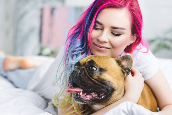 beautiful girl laying in bed and hugging cute french bulldog 