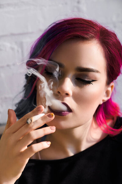 portrait shot of attractive girl with colorful hair holding joint with medical cannabis and smoking