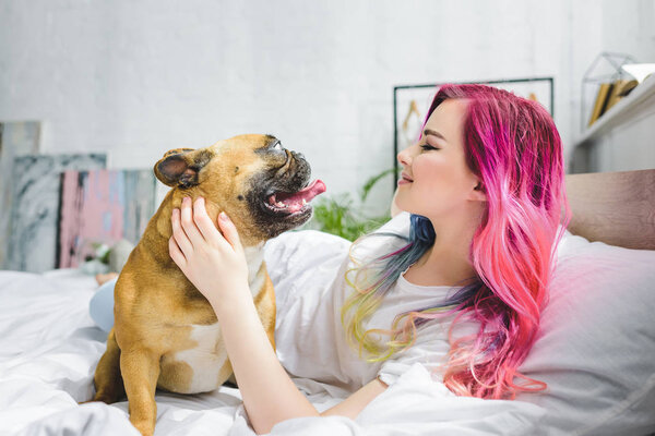 side view of attractive girl laying in bed and looking at french bulldog 