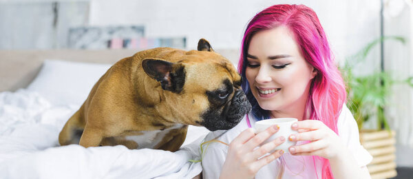 panoramic shot of happy girl with colorful hair holding cup with coffee and cute bulldog sniffing coffee